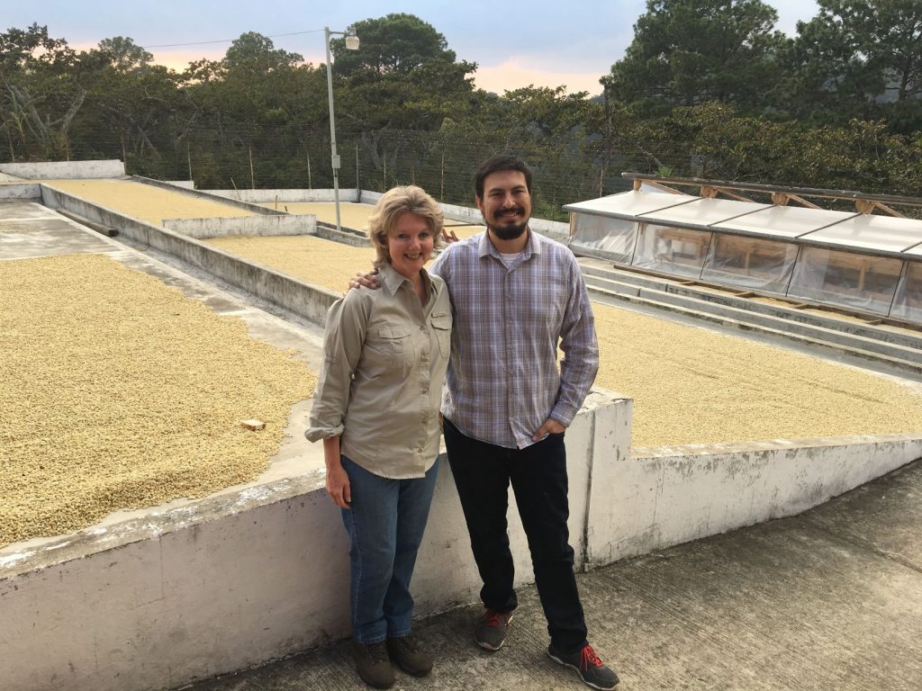 Two people posing in front of coffee bean drying beds
