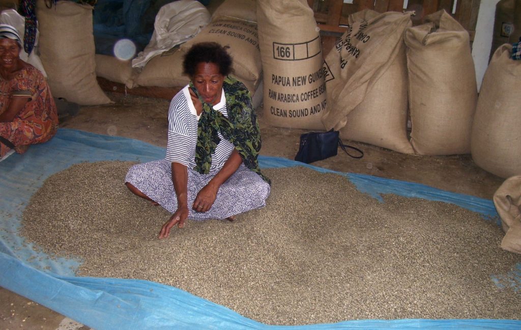 Worker sitting in a pile of dried coffee beans surrounded by full burlap sacks