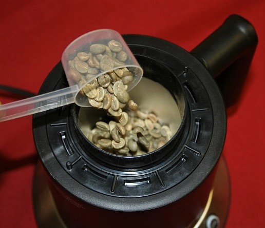 Green coffee beans being scooped into a Nesco Roaster
