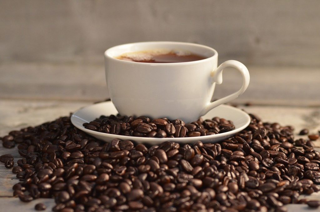 Coffee cup brewed with flavored coffee beans sitting on top of pile of beans