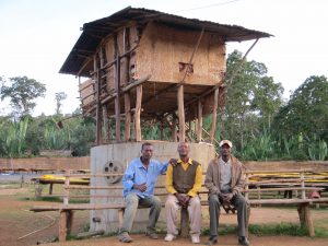 Three Ethiopian men sitting on a bench in front of a hut on stilts