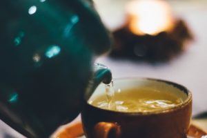 Teapot pouring hot water over tea to gain health benefits of green tea.