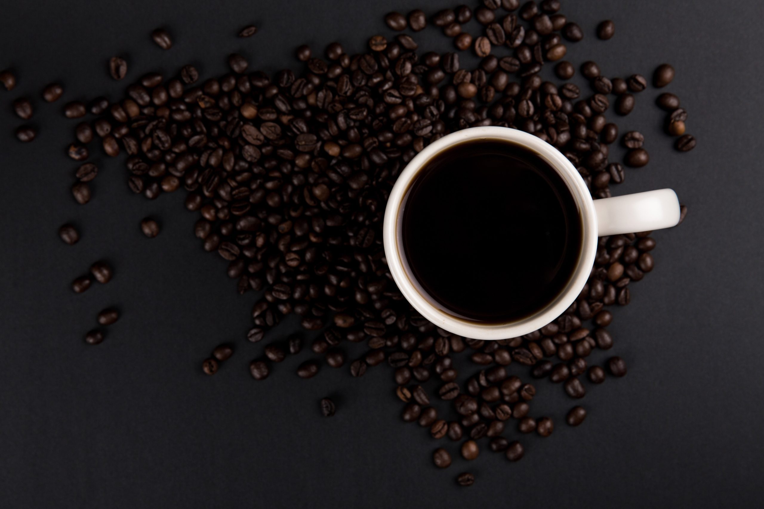 Cup of dark roasted coffee surrounded by coffee beans