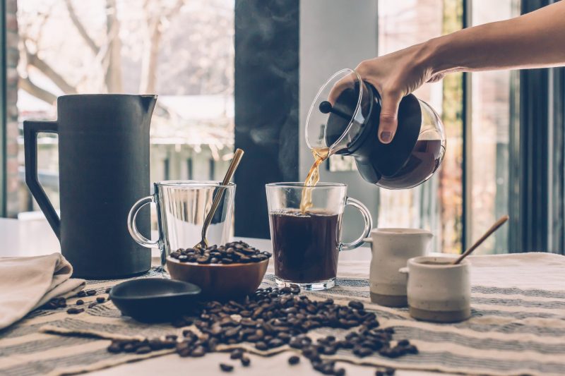 Woman pouring coffee into cup with coffee beans, sugar, and cream on table